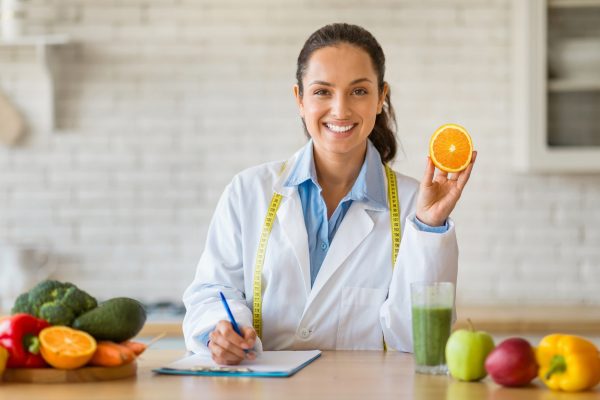 Dietician with orange in kitchen, writing nutrition plan